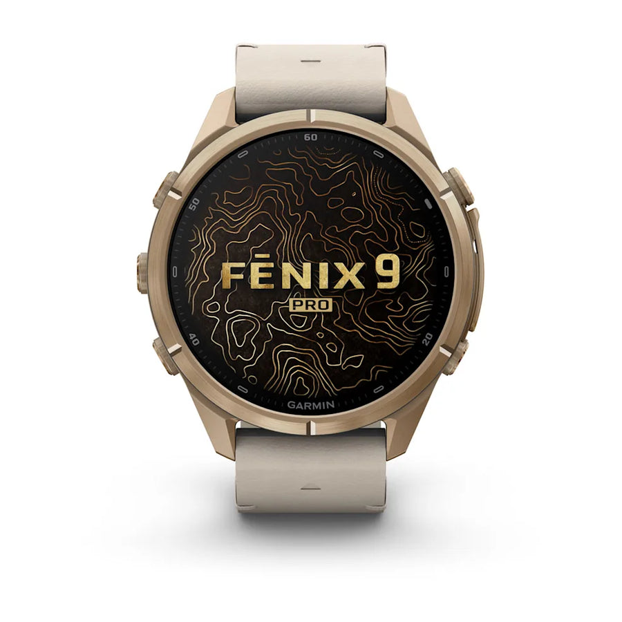 A Garmin Fenix 9 Pro smartwatch with a round metallic champagne-gold case, a light beige silicone strap, and a black display screen featuring gold topographic lines and the text 'FENIX 9 PRO'.