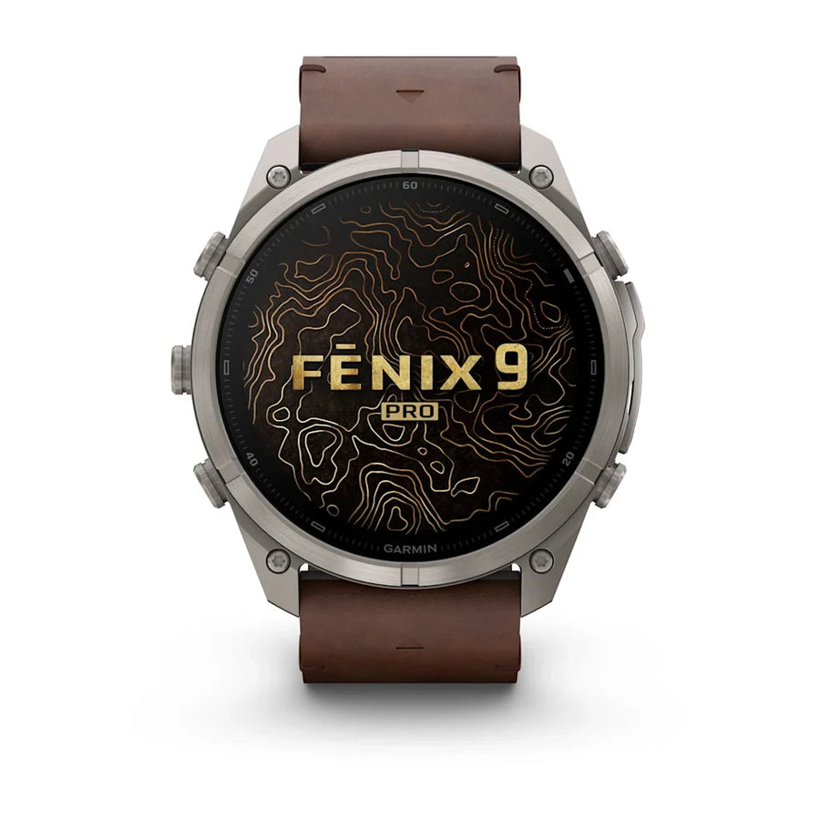 A Garmin Fenix 9 Pro smartwatch with a round silver-toned metal case and a brown leather strap, shown against a plain white background. The watch face displays a black background with gold topographic lines and the text 'FENIX 9 PRO'.