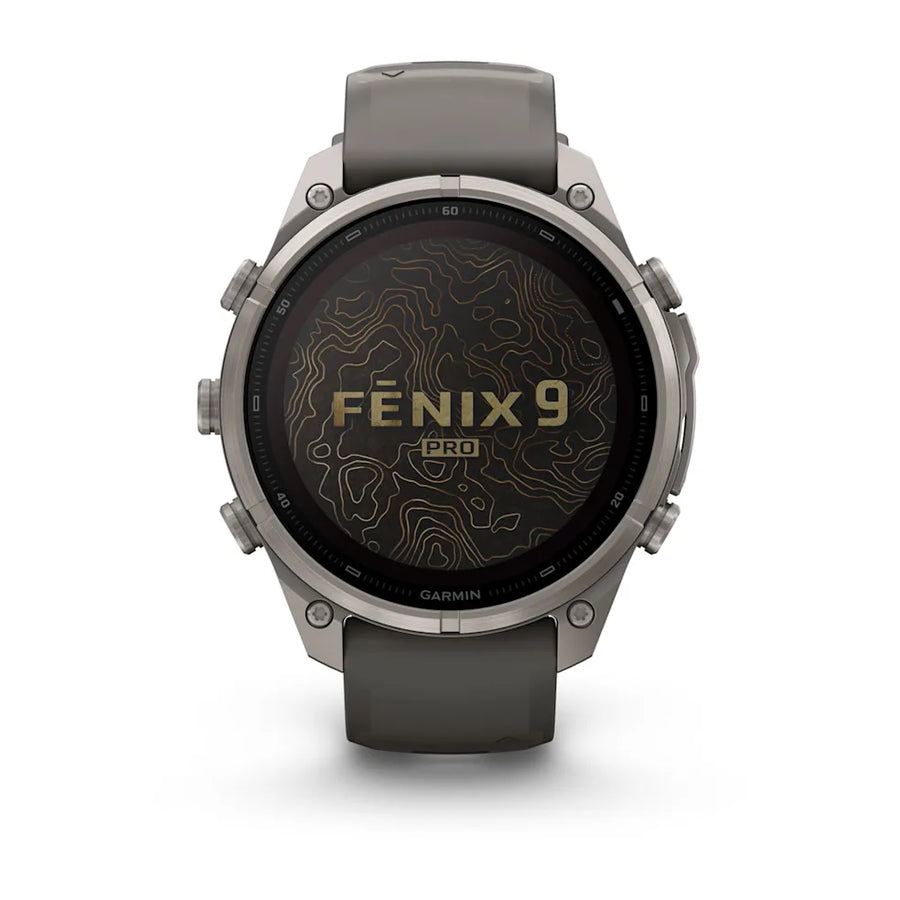 A Garmin Fenix 9 Pro smartwatch with a dark gray silicone strap and a silver-toned titanium case, shown against a clean white background. The watch face displays a black background with gold topographic contour lines and the text 'FENIX 9 PRO'.